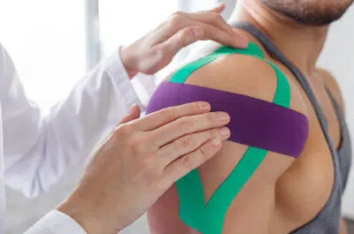 Épaule avec bandes de taping violet et vert – fracture de la tête humérale | IK Kiné et Balnéo