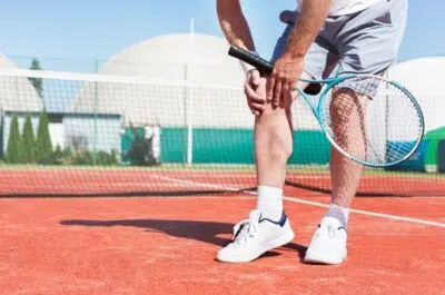Tennisman se tenant le genou sur un court – tendinite, entorse ou déchirure | IK Kiné et Balnéo